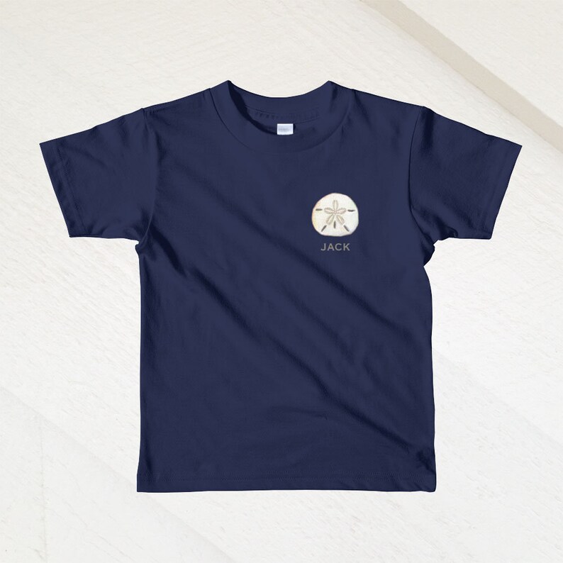 K&ouml;nnte beinhalten: Ein marineblaues T-Shirt mit einem wei&szlig;en Sanddollar-Motiv und dem Namen "JACK" darunter.