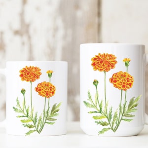 May include: Two white ceramic mugs with a floral design. The mugs feature orange and yellow marigold flowers with green stems and leaves.