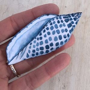 May include: A blue and white seashell with a patterned design. The shell is held in a hand.