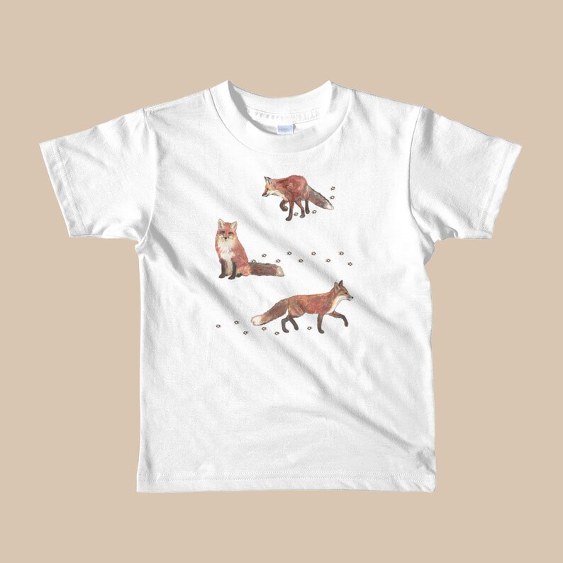 May include: White t-shirt with a graphic of three red foxes walking on a white background with small black paw prints.