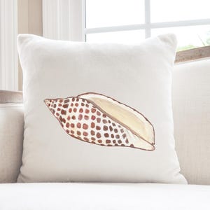 May include: White throw pillow with a brown and white seashell illustration.