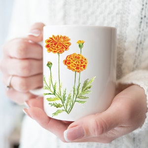 May include: White ceramic mug with a watercolor illustration of orange marigolds with green stems and leaves.