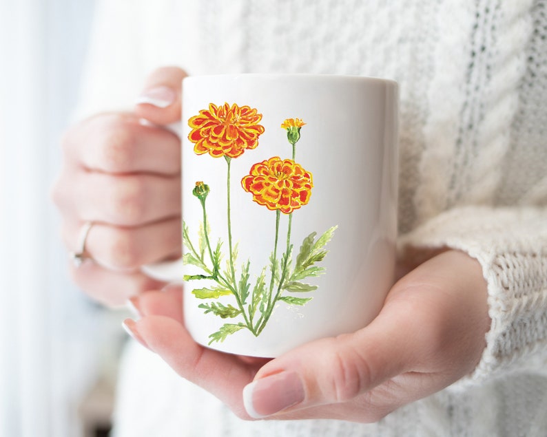 May include: White ceramic mug with a watercolor illustration of orange marigolds with green stems and leaves.