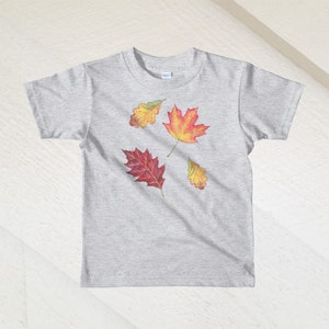 以下が含まれることがあります： ヘザーグレーのTシャツに、赤、オレンジ、黄色の4枚の秋の葉のデザインが施されています。