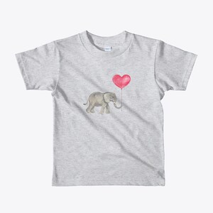 K&ouml;nnte beinhalten: Ein graues T-Shirt mit einer Aquarell-Illustration eines grauen Elefanten, der einen roten herzf&ouml;rmigen Ballon h&auml;lt.