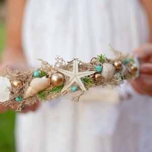 May include: A white starfish, seashells, and turquoise beads are woven into a brown moss base to create a whimsical crown.