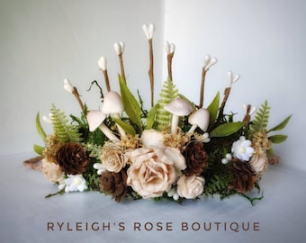 May include: A woodland-themed crown made of twigs, moss, and faux mushrooms. The crown is decorated with white and brown flowers and pine cones.
