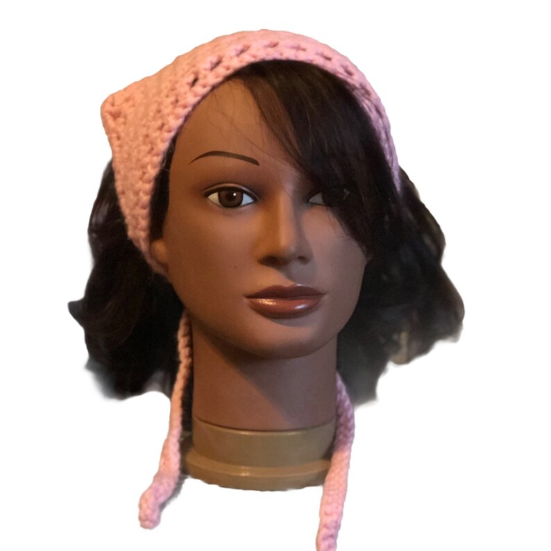 Op de afbeelding: Een roze gehaakt hoofdband met lange banden. De hoofdband wordt gedragen door een mannequin met bruin haar.