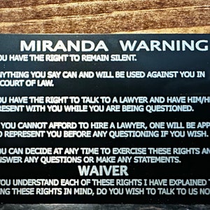 Może przedstawiać: Czarna karta z białym tekstem opisującym prawa z ostrzeżenia Miranda. Karta zawiera tekst "Miranda Warning" u g&oacute;ry i "WAIVER" na dole. Tekst brzmi: "Masz prawo do zachowania milczenia. Wszystko, co powiesz, może być wykorzystane przeciwko Tobie w sądzie. Masz prawo do rozmowy z adwokatem i do jego obecności podczas przesłuchania. Jeśli nie możesz sobie pozwolić na wynajęcie adwokata, zostanie Ci przydzielony adwokat do reprezentowania Cię przed jakimkolwiek przesłuchaniem, jeśli tego chcesz. Możesz w każdej chwili zdecydować się na skorzystanie z tych praw i nie odpowiadać na żadne pytania ani składać żadnych oświadczeń. WAIVER. Czy rozumiesz każde z tych praw, kt&oacute;re Ci wyjaśniłem? Mając na uwadze te prawa, czy chcesz porozmawiać z nami teraz?"