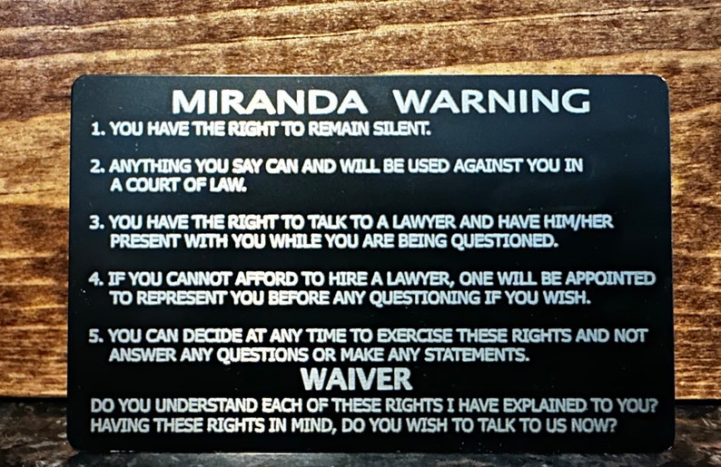 Może przedstawiać: Czarna karta z białym tekstem opisującym prawa z ostrzeżenia Miranda. Karta zawiera tekst "Miranda Warning" u g&oacute;ry i "WAIVER" na dole. Tekst brzmi: "Masz prawo do zachowania milczenia. Wszystko, co powiesz, może być wykorzystane przeciwko Tobie w sądzie. Masz prawo do rozmowy z adwokatem i do jego obecności podczas przesłuchania. Jeśli nie możesz sobie pozwolić na wynajęcie adwokata, zostanie Ci przydzielony adwokat do reprezentowania Cię przed jakimkolwiek przesłuchaniem, jeśli tego chcesz. Możesz w każdej chwili zdecydować się na skorzystanie z tych praw i nie odpowiadać na żadne pytania ani składać żadnych oświadczeń. WAIVER. Czy rozumiesz każde z tych praw, kt&oacute;re Ci wyjaśniłem? Mając na uwadze te prawa, czy chcesz porozmawiać z nami teraz?"