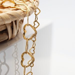 Könnte beinhalten: Eine goldene Kettenkette mit herzförmigen Gliedern. Die Kette liegt auf einem geflochtenen Korb.