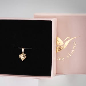May include: A gold heart pendant necklace in a black velvet box with a pink lid. The box has the text "My Lovers" printed on the lid.
