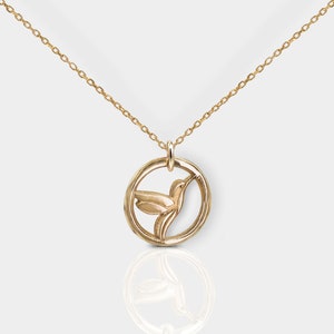 Pode incluir: Um colar de ouro com um pingente circular que apresenta um design detalhado de beija-flor.