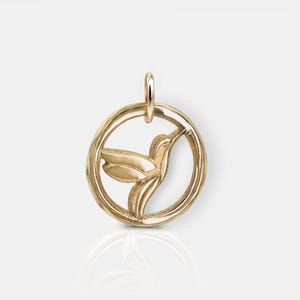 Pode incluir: Pingente de ouro com um beija-flor em voo, recortado de um design circular.
