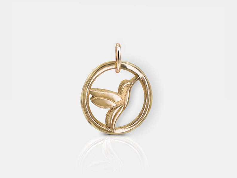Pode incluir: Pingente de ouro com um beija-flor em voo, recortado de um design circular.