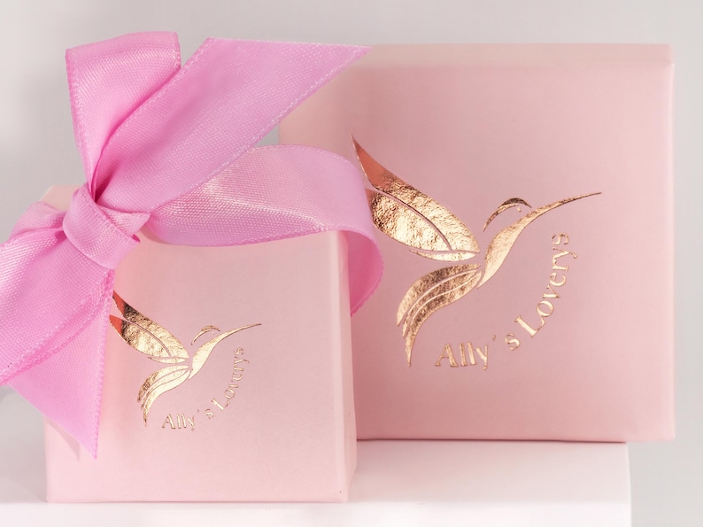 May include: Two pink gift boxes with a gold hummingbird logo and the text "Ally's Lovery's". The boxes are tied with a pink ribbon.