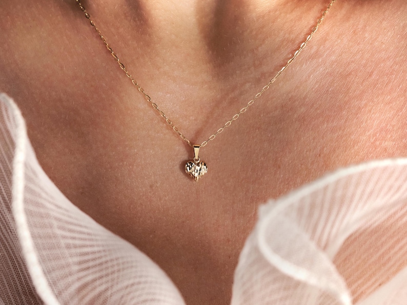May include: A delicate gold chain necklace with a small, textured heart pendant.
