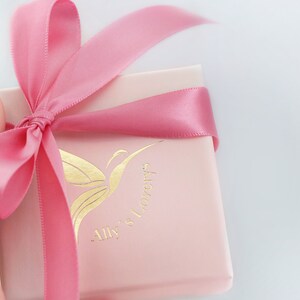 May include: A pink gift box with a pink satin ribbon tied in a bow. The box has a gold butterfly logo with the text "Ally's Lovery's".