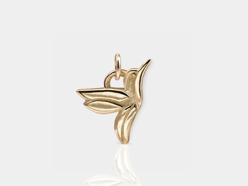 Pode incluir: Um pingente de beija-flor dourado. O beija-flor est&aacute; em voo com as asas abertas. O pingente tem um la&ccedil;o na parte superior para prender a um colar ou pulseira.
