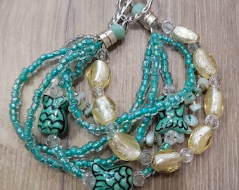 May include: A multi-strand bracelet featuring turquoise seed beads, clear crystal beads, and gold-toned oval beads. The bracelet includes turquoise fish-shaped beads with black detailing and a silver-toned toggle clasp.