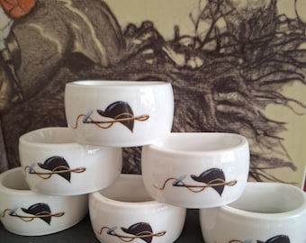 Juego de seis servilleteros de cerámica con motivos ecuestres. Representan sombreros de montar y fustas de caza. Cacería inglesa del zorro.