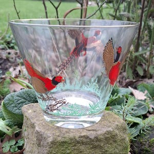 May include: A clear glass bowl with a gold rim, featuring a painted design of three red and brown pheasants in a green grassy field.
