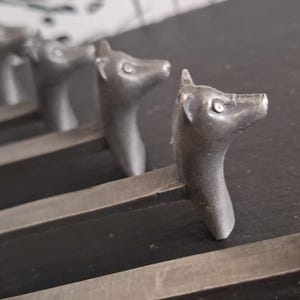May include: Close-up of several metal drawer pulls. Each pull is shaped like a deer head with a long neck. The pulls are a dark gray color and are mounted on a dark surface. The deer heads are facing different directions.