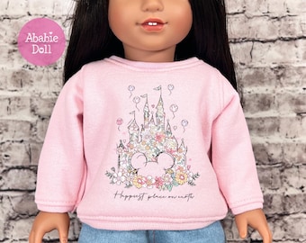 May include: A pink doll sweatshirt featuring a floral castle design with a Mickey Mouse silhouette and the text "Happiest place on earth." The sweatshirt is on a doll with black hair and blue jeans. A pink circle with the text "Ababie Doll" is in the upper left corner.