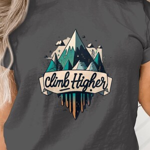 May include: Dark gray t-shirt featuring a mountain graphic with teal and blue accents. The design includes the text "Climb Higher" on a banner. The graphic has a retro, outdoorsy aesthetic.