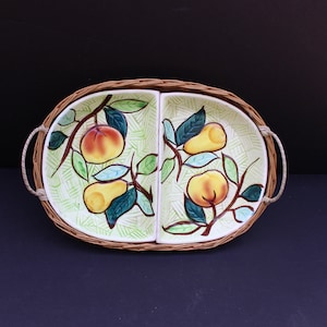 May include: Oval serving dish with two compartments, featuring a woven wicker border and rope handles. The ceramic interior is decorated with a fruit design of peaches and pears on a light green background.