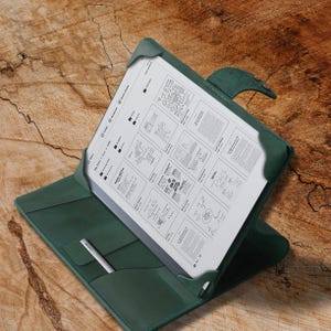 May include: A dark green leather folio case with a built-in pen holder. The case is open, revealing a white tablet with a handwritten document.