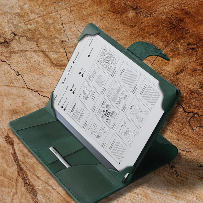 May include: A dark green leather folio case with a built-in pen holder. The case is open, revealing a white tablet with a handwritten document.