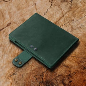 May include: A dark green leather notebook cover with two brass rivets and a flap closure.