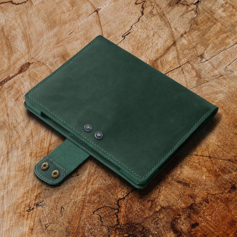 May include: A dark green leather notebook cover with two brass rivets and a flap closure.