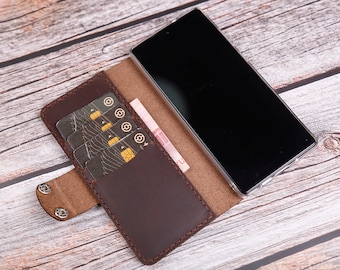 Op de afbeelding: Een bruine leren telefoonhoes met vakken voor creditcards en een flap die over het telefoonscherm vouwt.