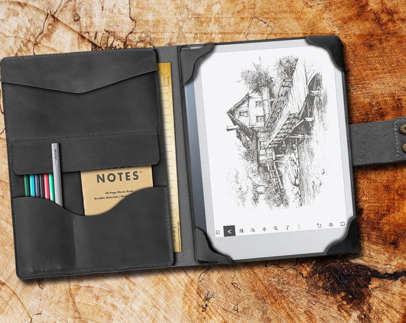 May include: A black leather folio case with a built-in notepad and pen holder. The case has a flap that closes with a magnetic snap. The case is open to reveal a black and white e-reader with a drawing of a house on a bridge. The text "NOTES" is visible on the notepad.