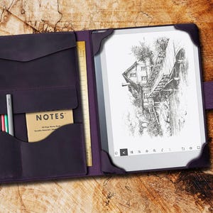 May include: A purple leather folio case with a built-in notepad and pen holder. The case is open to reveal a black and white e-reader with a drawing of a house on a bridge. The text "NOTES" is visible on the notepad.