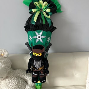 May include: A green and black school cone with a ninja figure attached. The cone has a white star with a black ninja symbol in the centre. The cone is decorated with green and black ribbons.