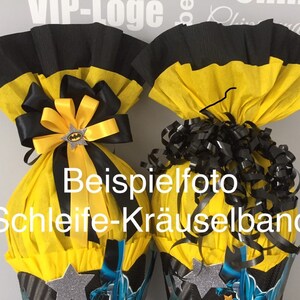 May include: Two yellow and black party cones with a Batman theme. One cone has a black and yellow bow with a Batman charm. The other cone has black curly ribbon. The cones are decorated with silver stars and a Batman graphic. The text "Beispielfoto Schleife-Kr&auml;uselband" is visible on the cones.