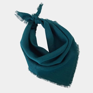 Può includere: Una bandana color verde acqua scuro di forma quadrata con bordi sfrangiati. Il tessuto è piegato e annodato sulla parte superiore, creando una silhouette triangolare drappeggiata. Il materiale presenta una trama tessuta visibile.