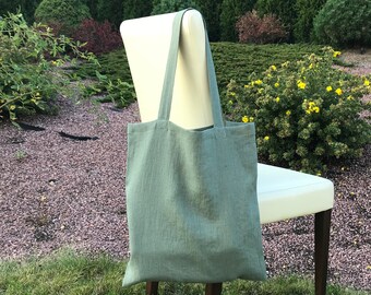 May include: A sage green linen tote bag with fabric handles hanging on a white chair in a garden setting.