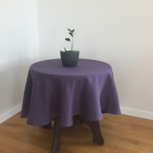 Peut inclure: Une nappe en lin violette sur une table ronde en bois avec une petite plante en pot dans un pot gris.