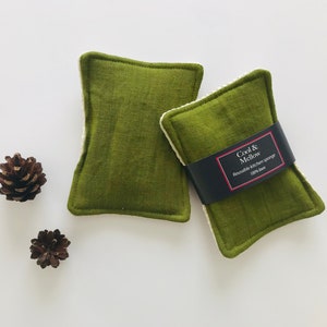 May include: Two green kitchen scrubbers with white edging. The scrubber on the right has a black label that reads "Cool & Mellow Reusable Kitchen Sponge 100% Linen".