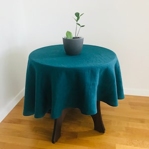 Könnte beinhalten: Tischdecke aus tealfarbenem Leinen auf einem runden Holztisch mit einer kleinen Topfpflanze in der Mitte.