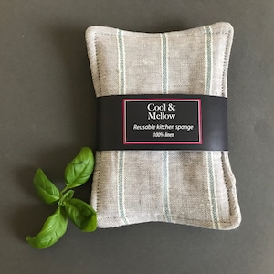 May include: A gray and white striped linen kitchen sponge with a black label that reads "Cool & Mellow Reusable kitchen sponge 100% linen".