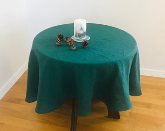 May include: A dark green linen tablecloth on a round table with a white candle and pine cones on top.