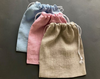 May include: Three drawstring bags made of natural linen fabric. The bags are in light blue, pink, and beige.