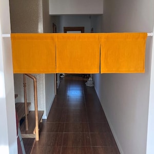 May include: A hallway entrance with a bright orange fabric valance hanging from a white rod. The hallway has dark wood flooring and white walls. A staircase is visible to the left.