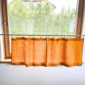 K&ouml;nnte beinhalten: Zwei orangefarbene Vorh&auml;nge aus Leinen, die an einer silbernen Gardinenstange vor einem Fenster h&auml;ngen.