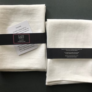 May include: Two white linen furoshiki wrapping cloths, one folded and one flat, with black labels that read "Cool & Mellow Furoshiki wrapping cloth".